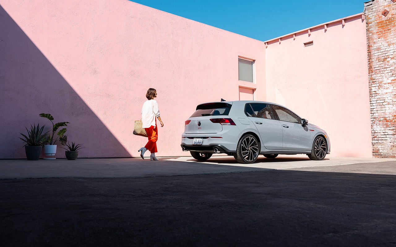 light grey Volkswagen Golf parked next to two pink walls with the driver walking towards it