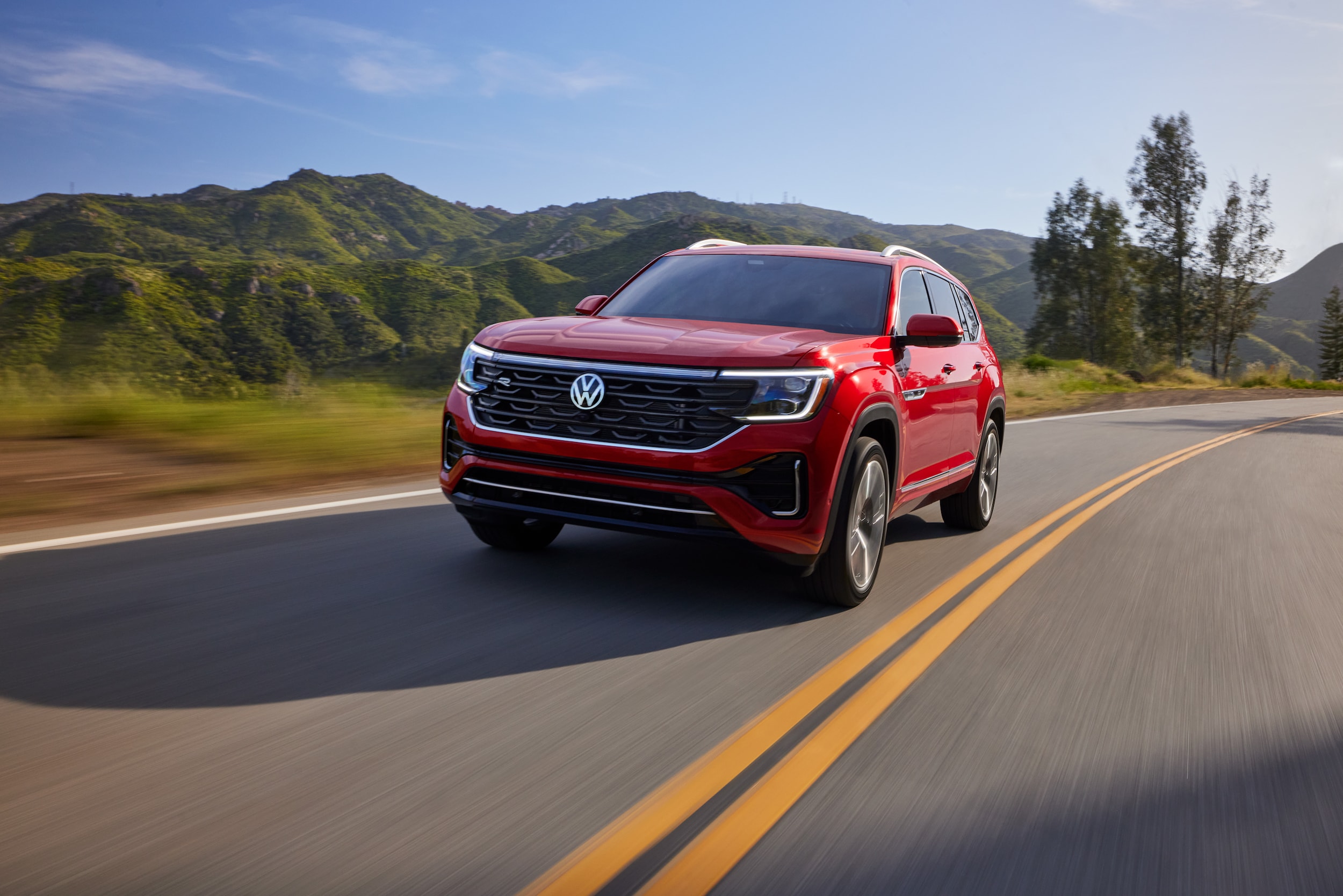 red Volkswagen Atlas driving past a background of green hills