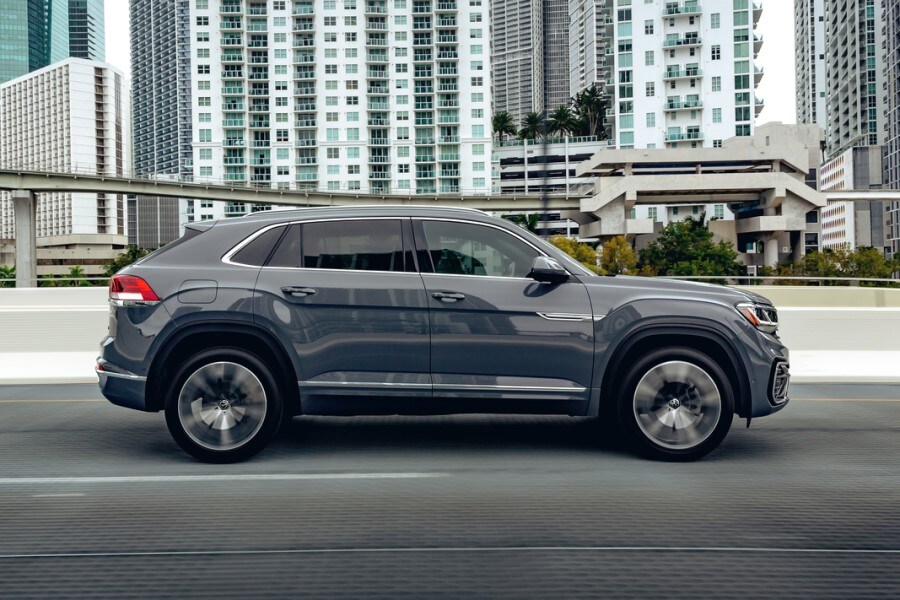 grey Volkswagen Atlas Cross Sport driving past large apartment buildings