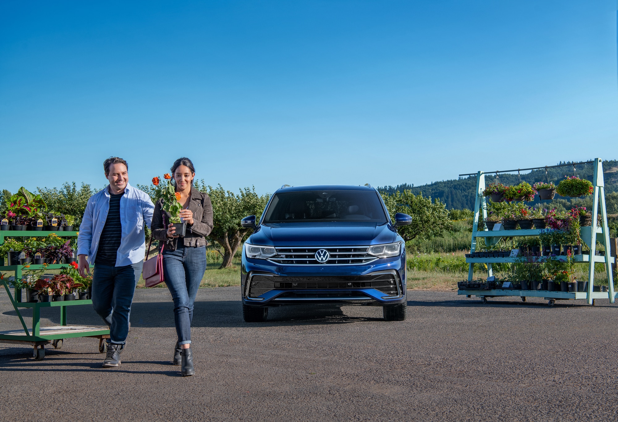 A new Volkswagen Tiguan in Atlantic Blue Metallic parked outdoors while a couple picks out flowers at a nursery in Berkshire County, MA.