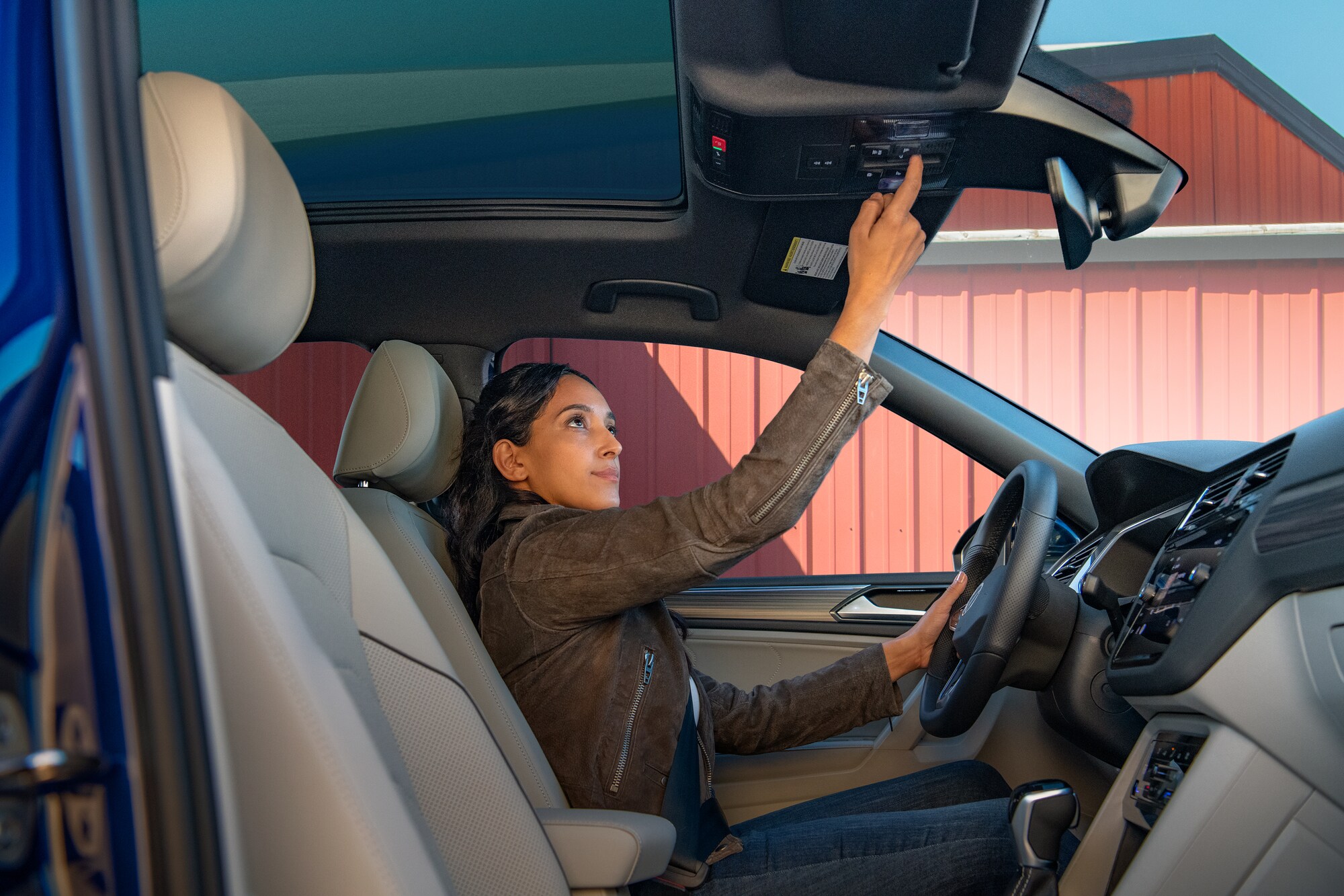 A woman opening the panoramic sunroof in her 2025 Volkswagen Tiguan