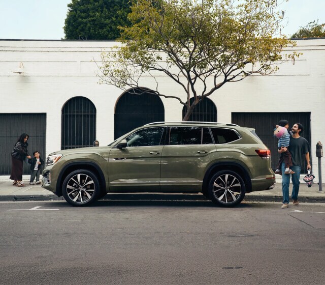 Exterior side image of a family near a green 2026 Volkswagen Atlas parked on a city street.
