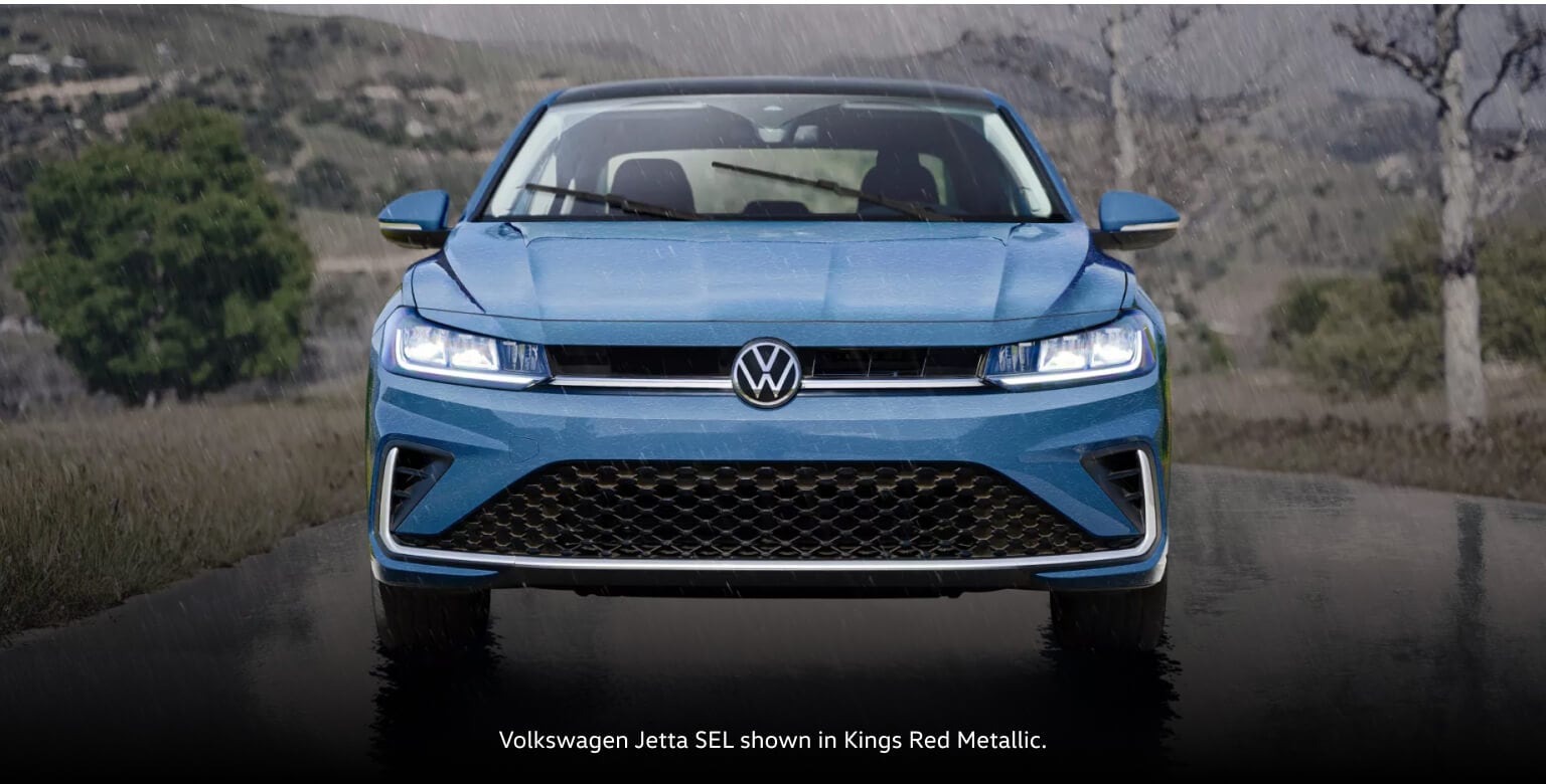 Front view of a 2027 Volkswagen Jetta SEL in Monterey Blue Pearl driving on a wet road.