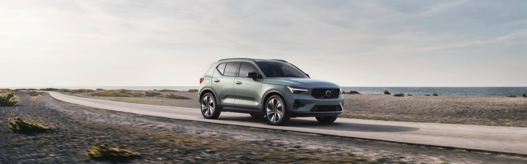 Low-Mileage Used Vehicles for Sale Volvo SUV driving along a coastal roadway showcasing low-mileage pre-owned vehicle options