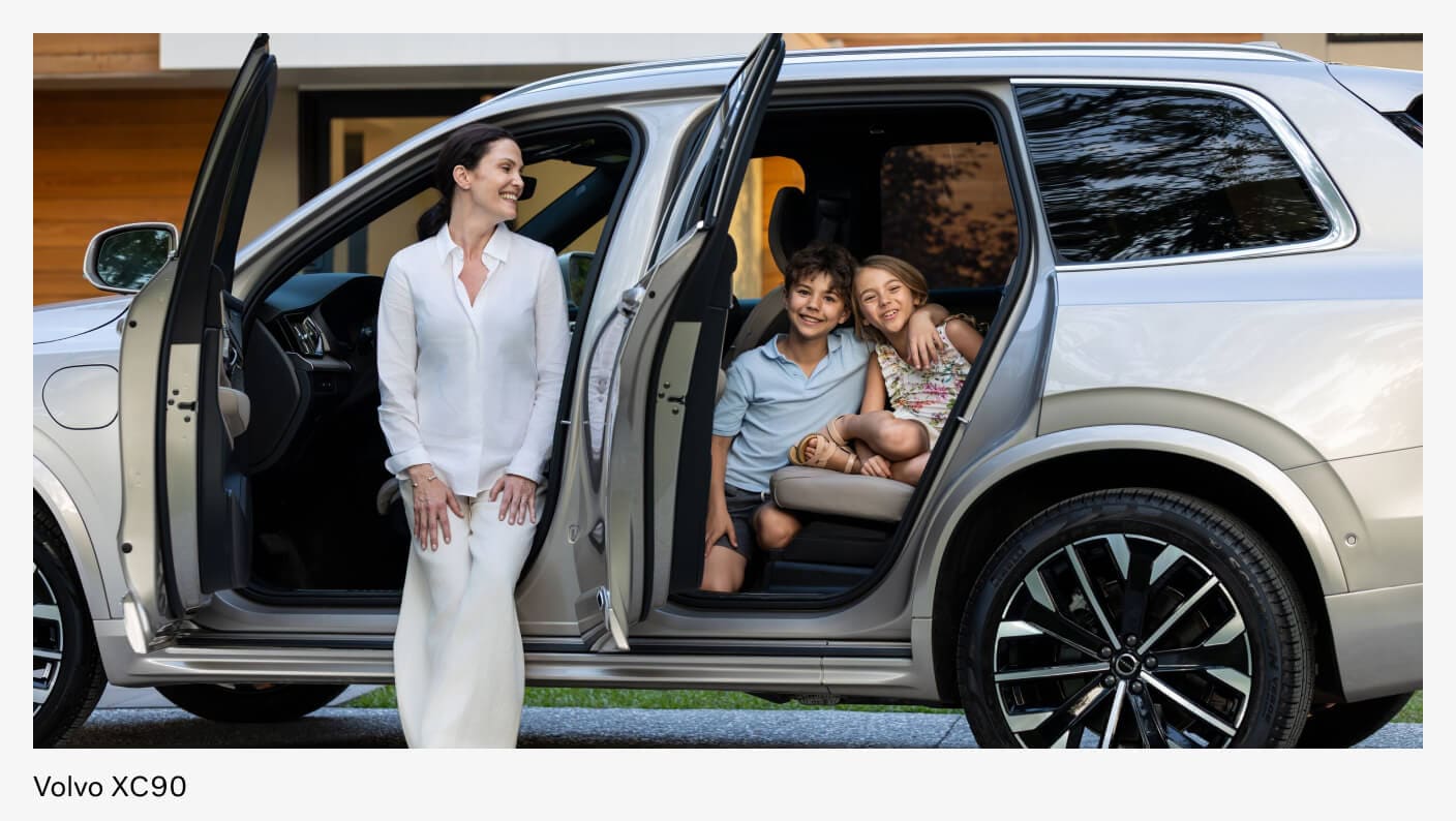 Exterior side view of a woman and her family smiling as they sit in their Volvo XC90.