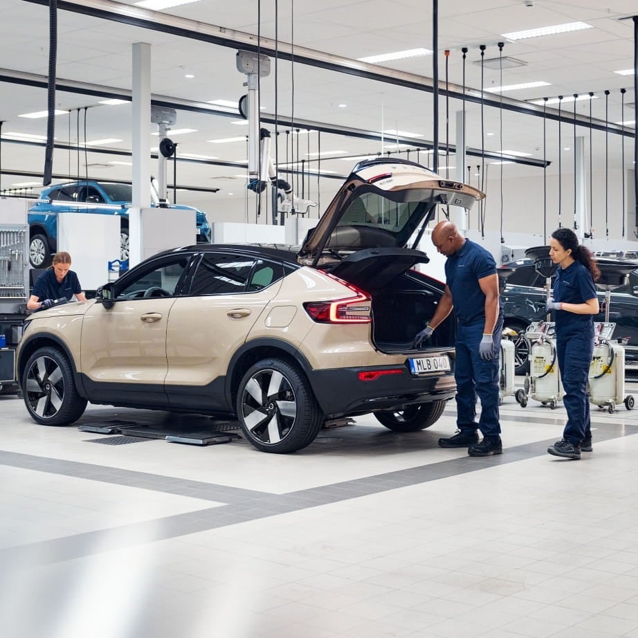 Mechanics in a Volvo workshop inspect an SUV with an open trunk.