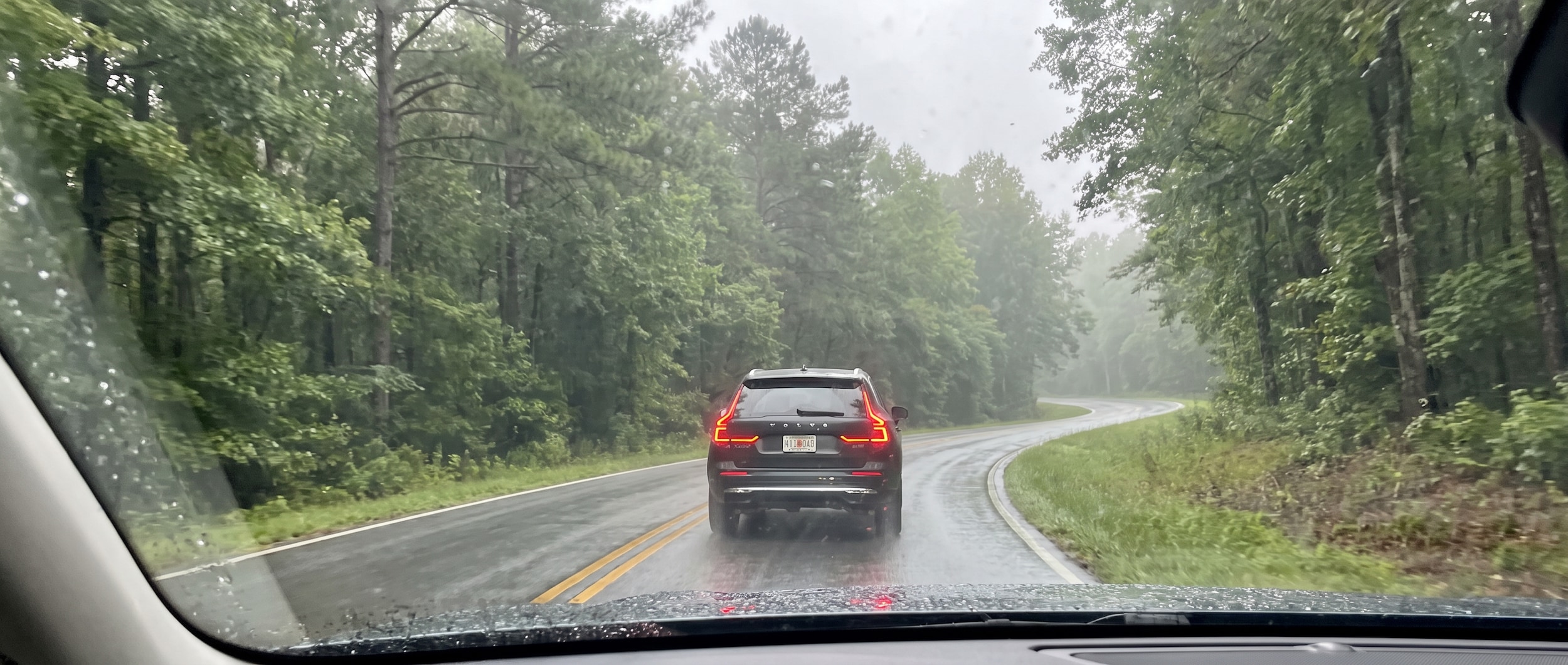2026 Volvo XC60 navigating a wet curve on a forested Upstate South Carolina road in summer rain