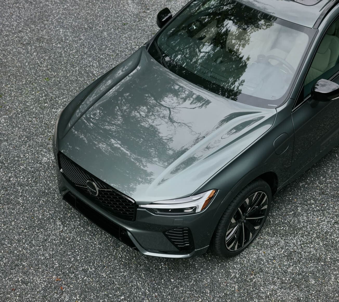 High-angle front view of a dark green Volvo XC60 SUV on a gravel surface.