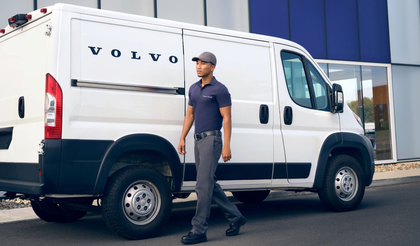 An exterior shot of a Volvo van parked outside of a Volvo Service Center with a Volvo Technician walking past.