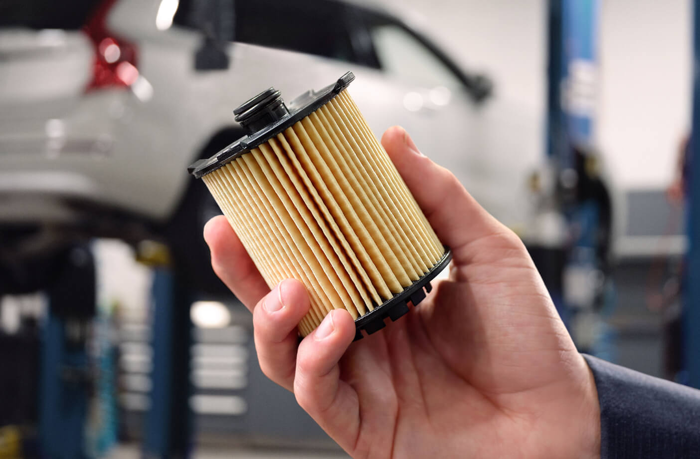 A close-up of a hand holding a Volvo oil filter inside a service center.