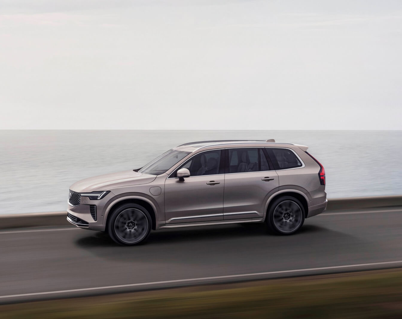 Side profile of a Bright Dusk Volvo XC90 driving along a coastal road.
