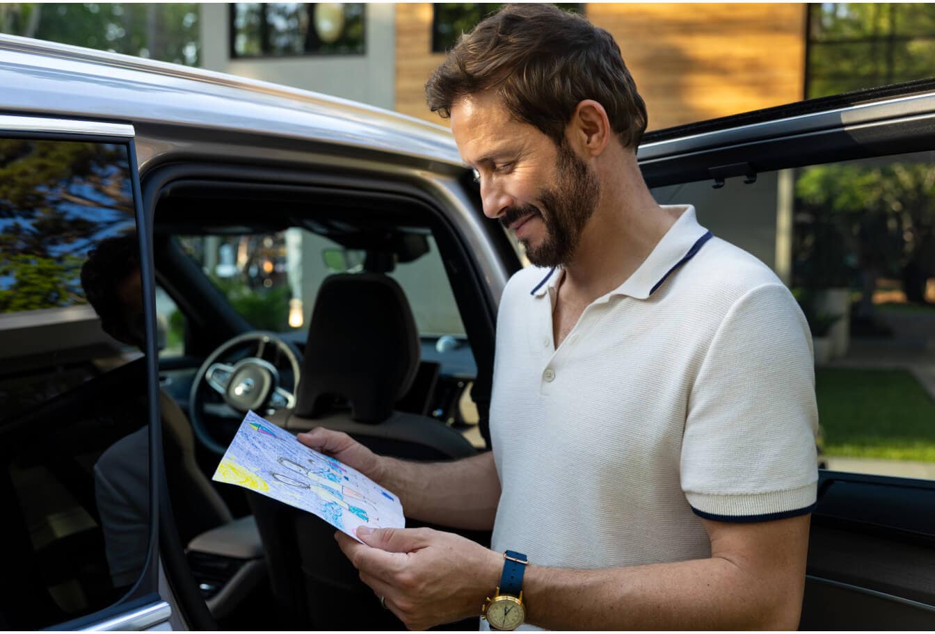 Side view of a father standing next to an open door of a Volvo XC90 looking down at a drawing.