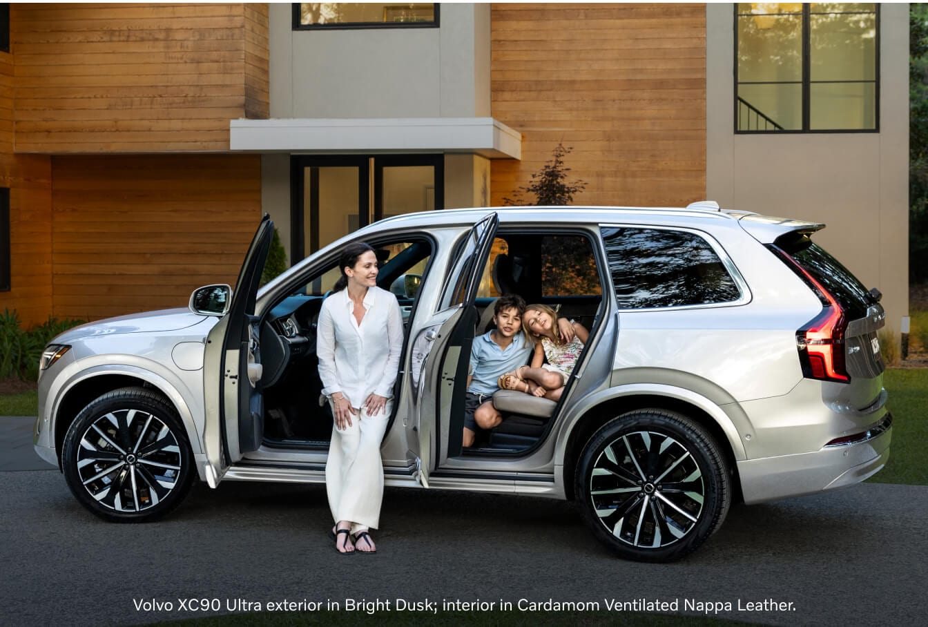 Side profile view of a Volvo XC90 with doors open posing with a family on a driveway.