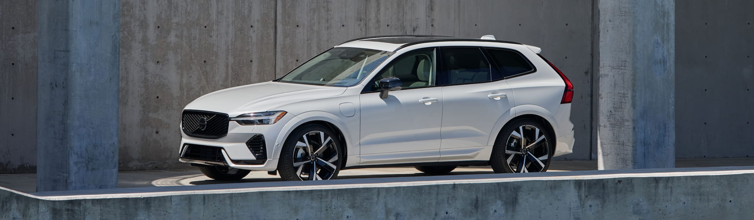 White Volvo XC60 SUV parked in front of a concrete wall.