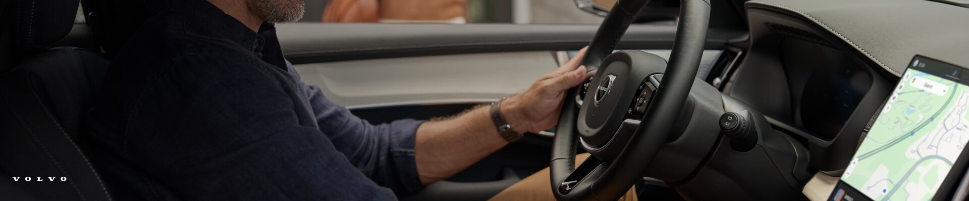 Driver perspective profile of a Volvo XC90 steering wheel and dashboard with a map on display.