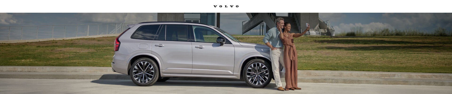 Volvo XC90 Ultra parked by a modern pavilion while a couple takes a selfie.