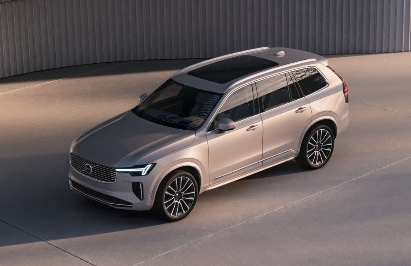 Volvo XC90 SUV shown from an elevated front three-quarter view in a modern outdoor setting.