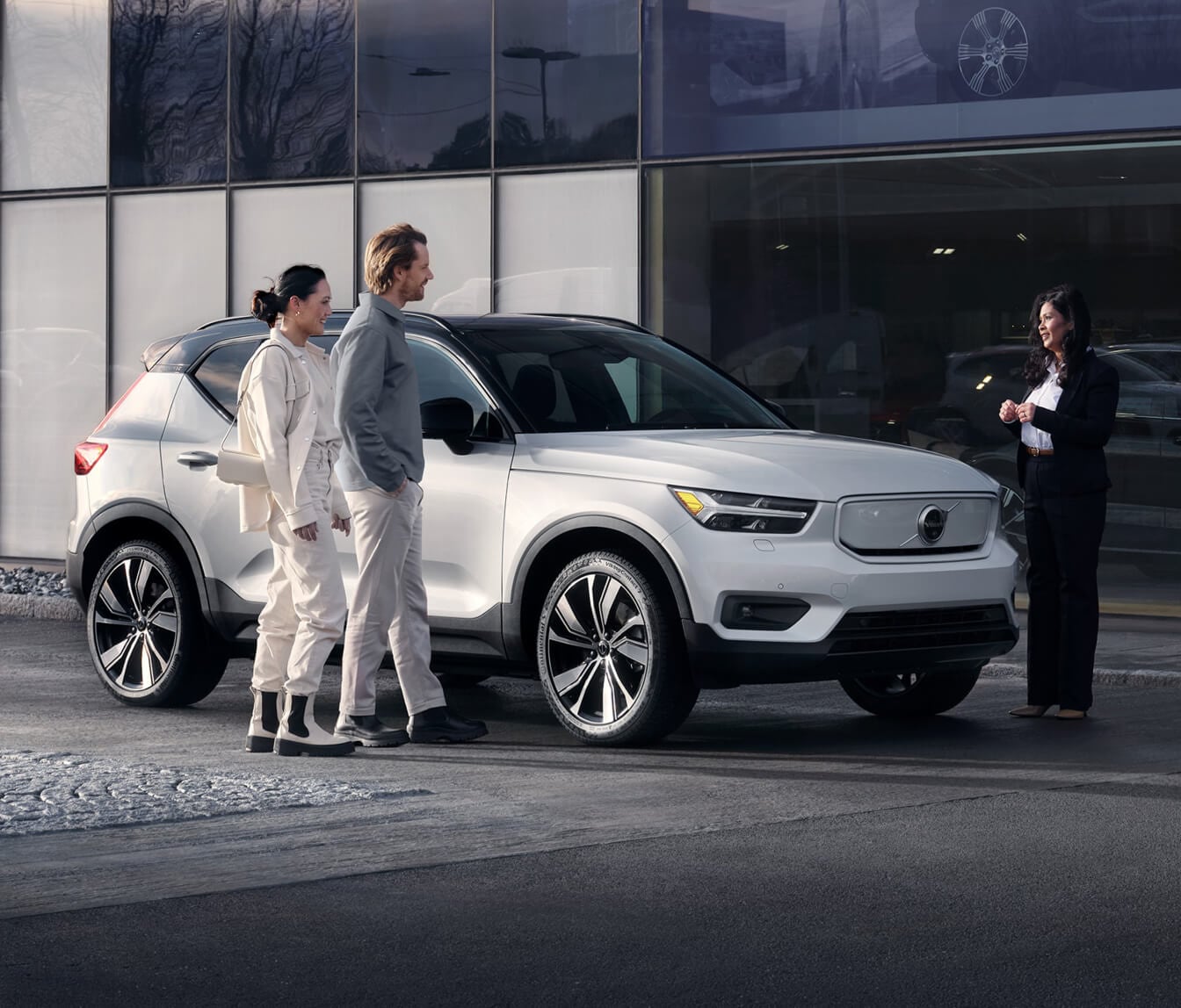 Front three-quarter view Volvo EX40 in Crystal White Metallic during a sales handover in front of a modern dealership showroom.