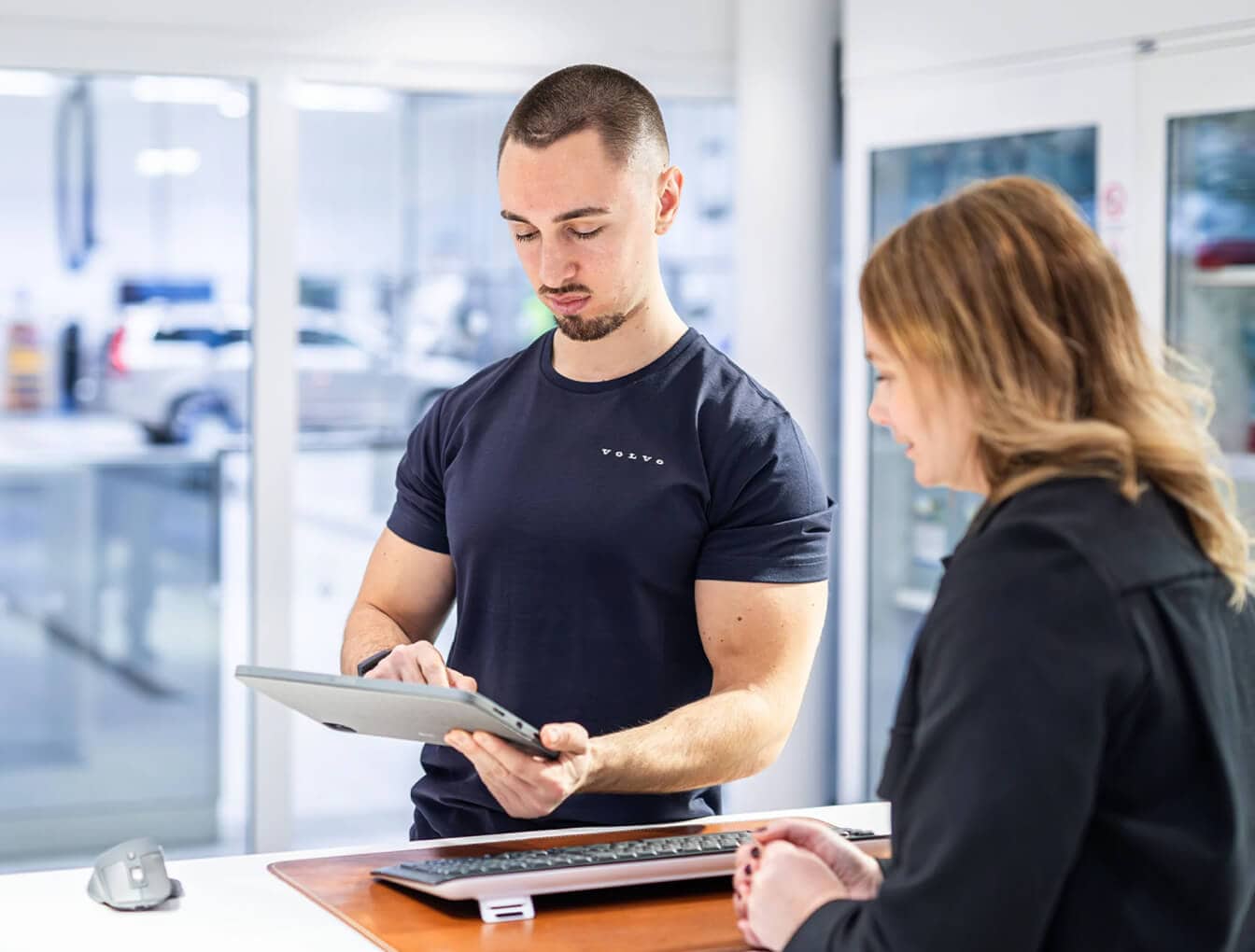 Close-up of a Volvo service technician using a digital tablet to review vehicle diagnostics with a customer at a white counter.