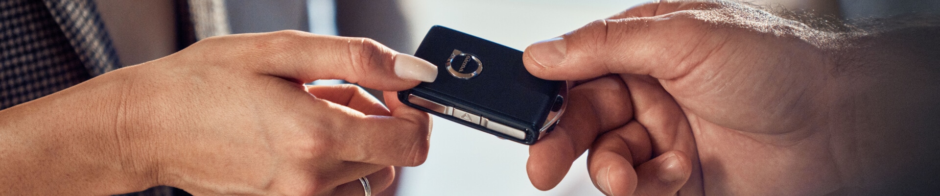 Close-up of two people exchanging a Volvo key fob during a vehicle handoff.