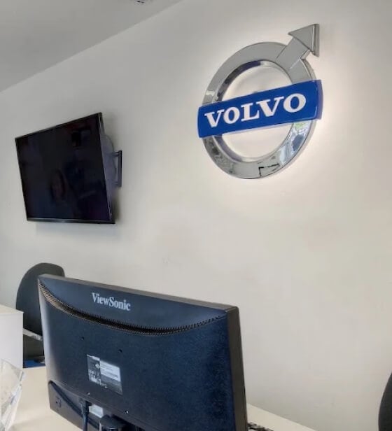 Volvo logo mounted on a white wall above an office desk monitor.