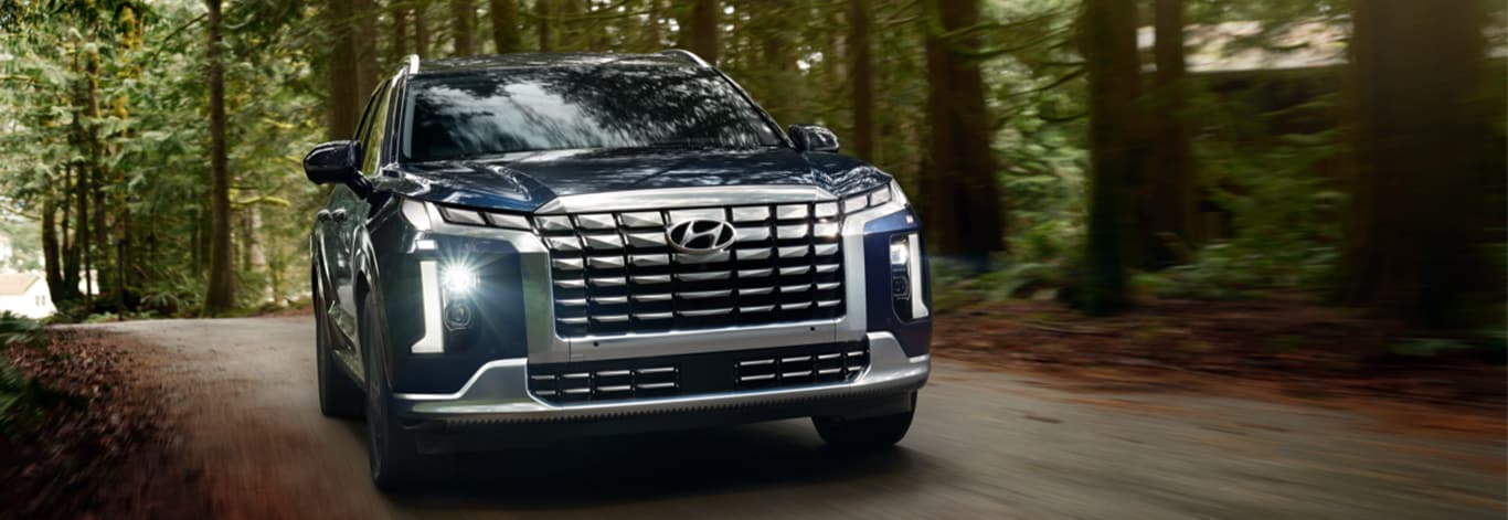 All-New 2023 Hyundai Palisade at West Broad Hyundai | Front view of a Navy blue Hyundai Palisade driving down a road with trees around it
