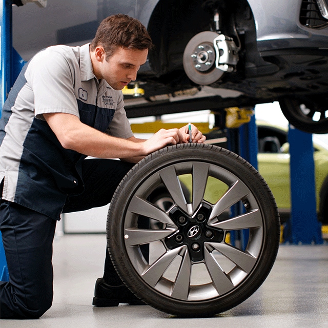 Basic Car Maintenance and Servicing Checklist | West Broad Hyundai | Hyundai Technician Squated Down Checking Tire Tread on a Detached Tire