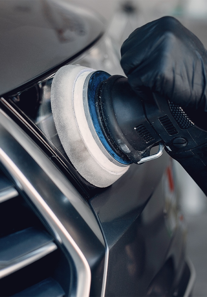 When to Trade In Your Car | West Broad Kia in Henrico, VA | Person with black gloves buffing grey car headlights by using a buffer