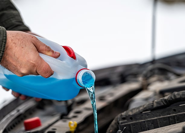How to prepare your Kia for the winter season in Henrico, VA at West Broad Kia | Man pouring blue windshield wiper fluid into engine bay 