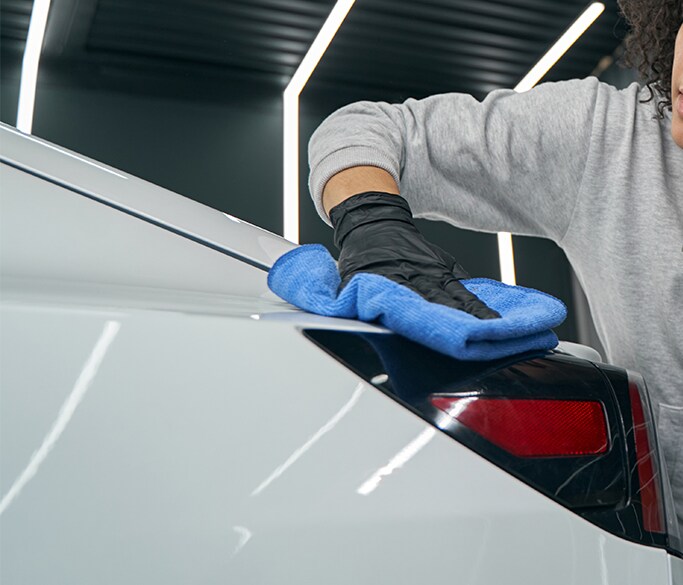 What is Paintless Dent Repair? | West Broad Kia | Person wiping down a white car with a blue cloat