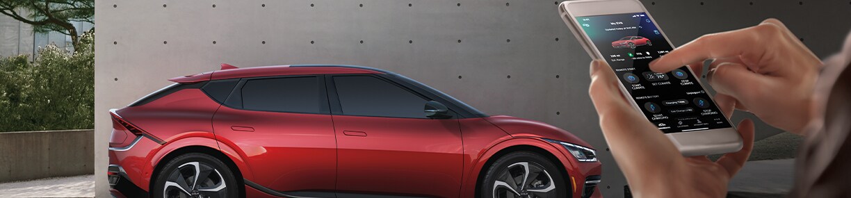 How to prepare your home for your new Electric Vehicle at West Broad Kia in Henrico, VA | Side view of a red 2023 Red Kia EV6 with a person checking the car battery life with his smart phone 