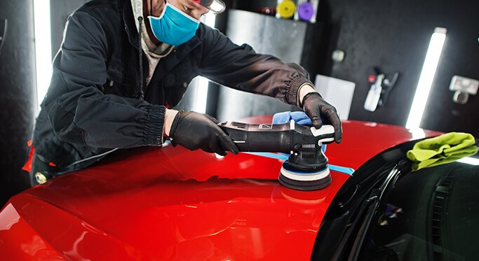 How to Get Your Car Summer Ready at West Broad Kia in Henrico, VA | Person in black uniform, wearing a mask and gloves, detailing red car with a polisher