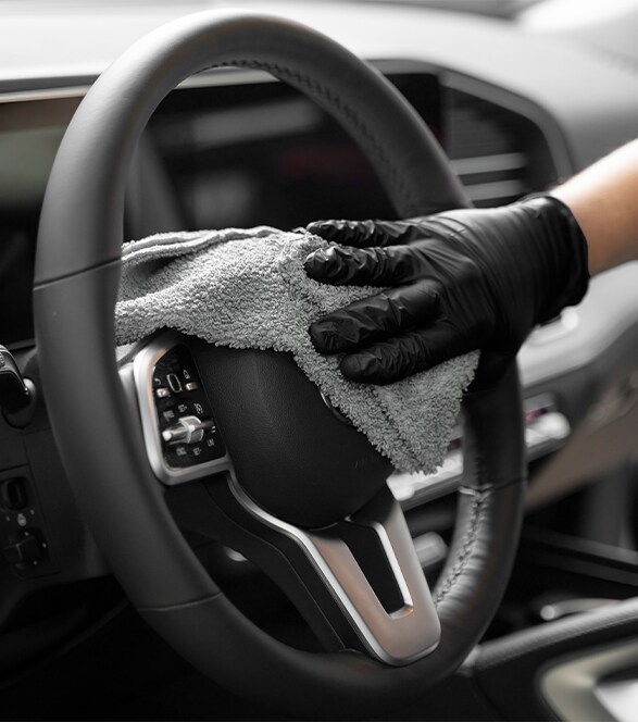 Person with black gloves cleaning steering wheel with cloth 