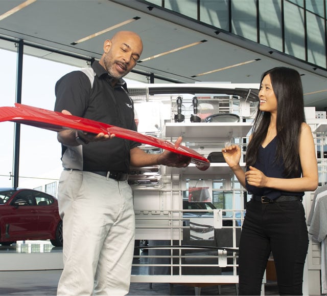 Accessories that help keep your Kia protected at West Broad Kia in Richmond, VA | Service Technician and Customer Looking at Red Car Bumper Together and Talking