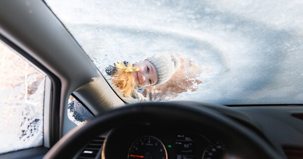 How to prepare your Kia for the winter season in Henrico, VA at West Broad Kia | View of drivers seat looking at the front windshield while it defrosts and a child head is looking in the defrost section