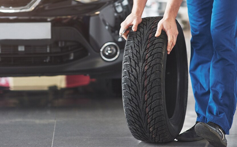 Extend the Life of Your Vehicle at West Broad Kia in Henrico, VA | Man with blue pants is rolling used tire on the ground 