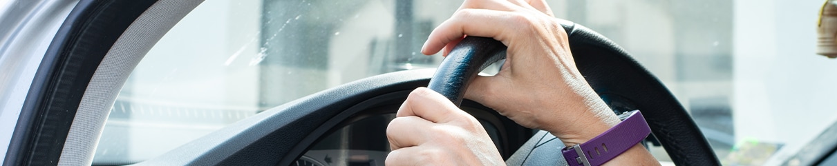 Learn Maintenance Warning Signs at West Broad Kia in Henrico, VA | A person wearing a purple watch has both hands on the steering wheel of her car  