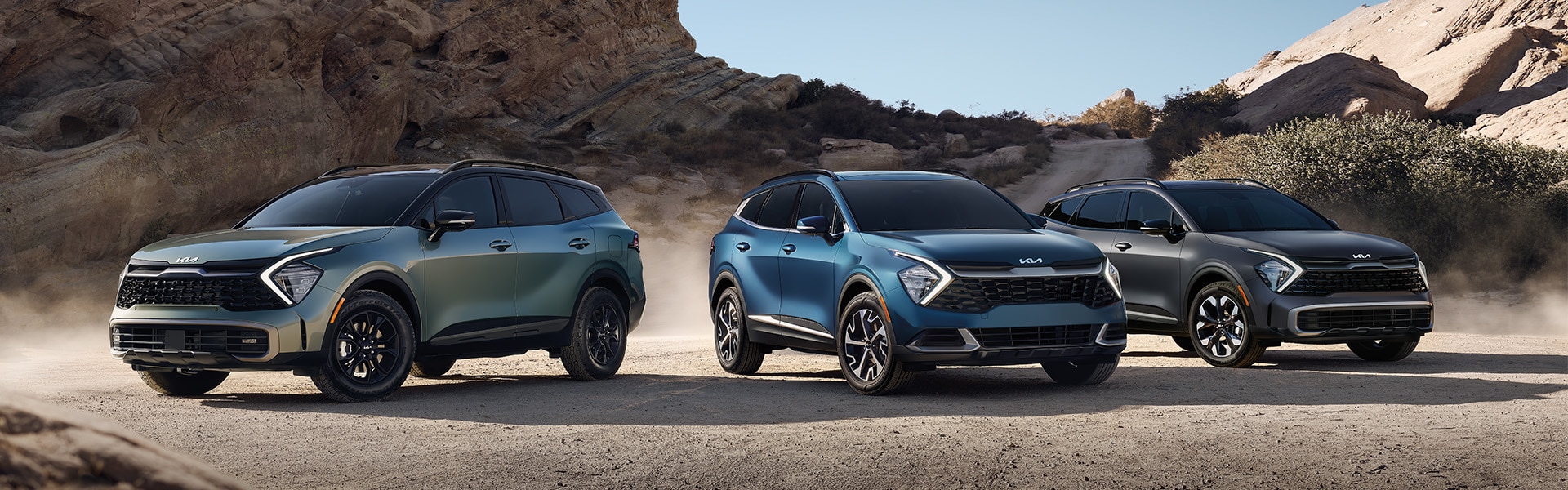 The All-New 2023 Kia Sportage at West Broad Kia in Henrico, VA | Green, Blue & Dark Silver 2023 Kia Sportage Vehicles Parked in Desert in Front of Rock Formation