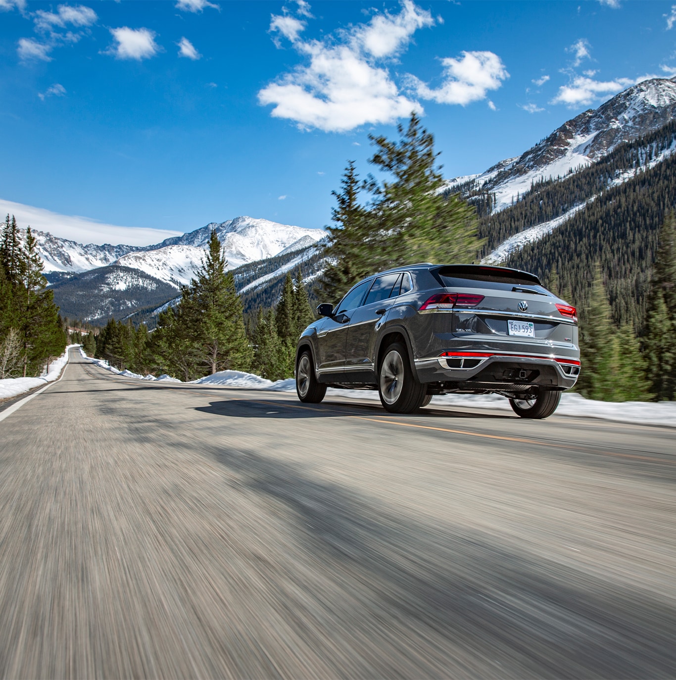 Model Features of the 2022 Volkswagen Atlas at West Broad Volkswagen | Rear view of a Matte Grey Volkswagen Atlas driving on the road with mountains and tall trees in the background
