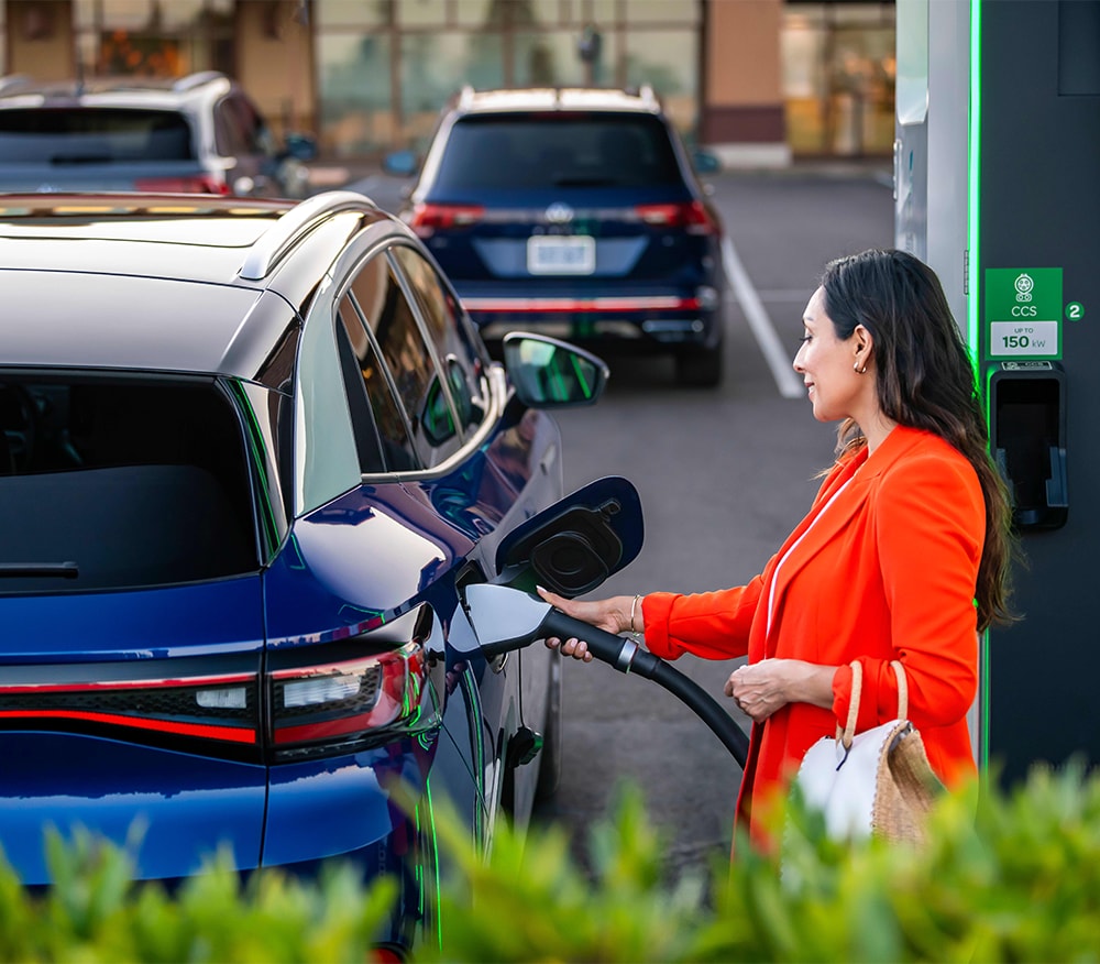 2023 ID.4 Electric SUV at West Broad VW | Woman in orange suit on the right plugging in car charger to a Navy blue 2023 Volkswagen ID.4 
