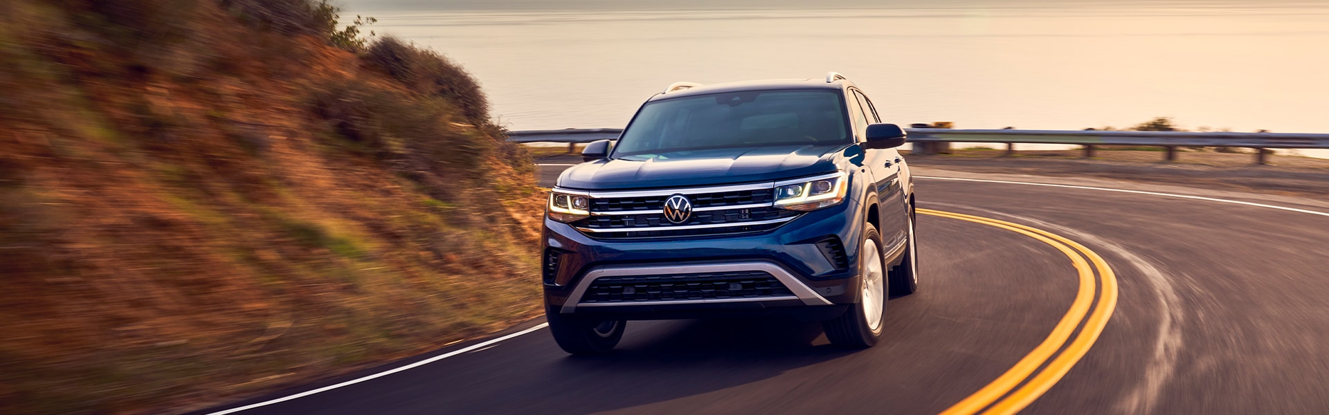 Compare the 2021 Volkswagen Atlas vs. the 2021 Ford Escape at West Broad Volkswagen | Blue 2021 Volkswagen Atlas Driving Around Bend at Sunset