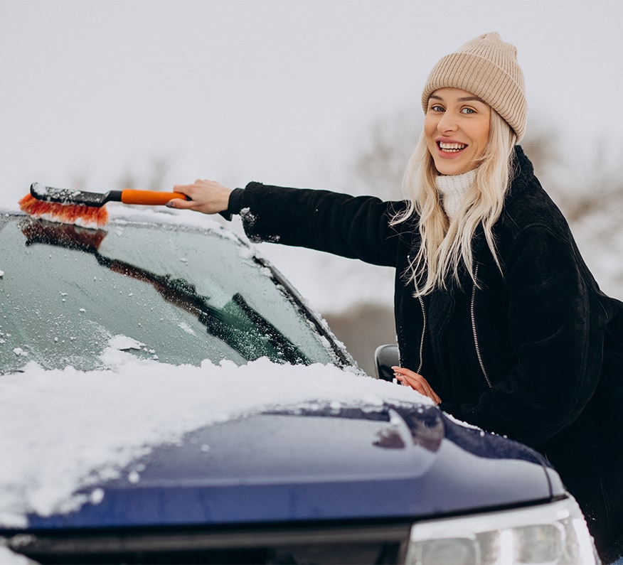 How to Prevent your Vehicle from Fogging Up At  West Broad VW in Richmond, VA | Woman in black jacket is cleaning the windshield of her car by using a orange brush 