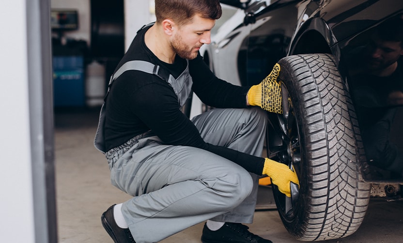 Extend the Life of Your Vehicle at West Broad VW in Richmond, VA | Mechanic with grey uniform and yellow gloves is installing tire on a black sedan car