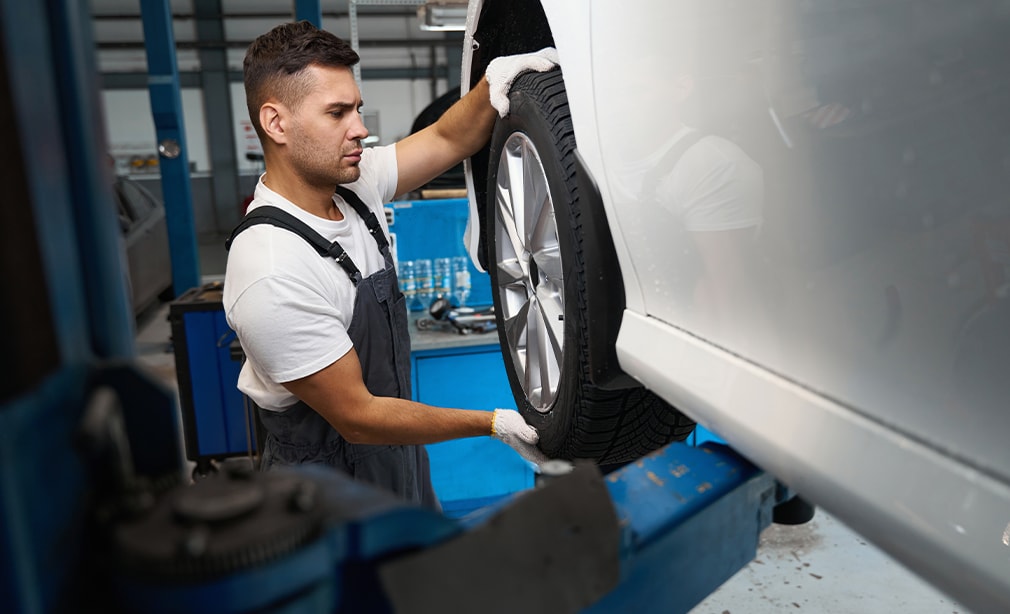Learn Maintenance Warning Signs at West Broad VW in Richmond, VA | Mechanic in white T-shirt and gloves is checking the car wheel for any shaking or vibration
