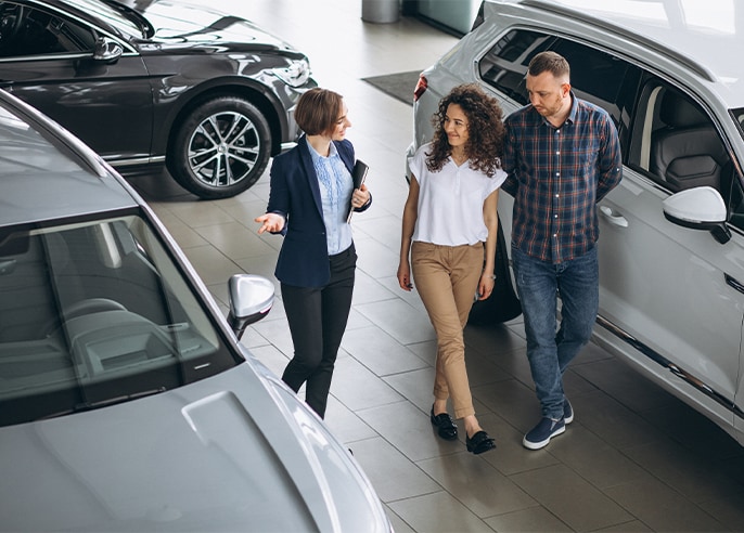 When to Trade In Your Car | West Broad VW in Richmond, VA | Salesperson wearing a navy blazer is showing cars in the showroom to a couple on the left side 