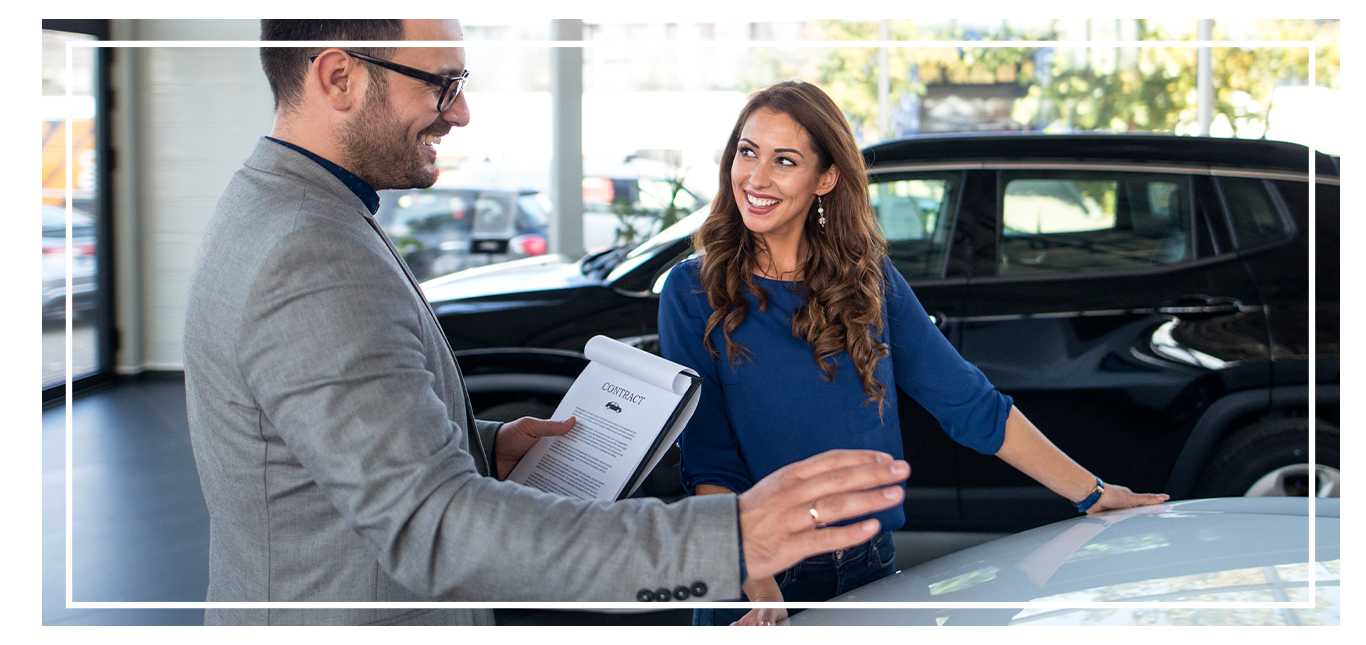 Things to Bring with you to Purchase a Car at West Broad Volkswagen in Richmond, VA | Sales person in grey suit is talking to customer about a new car while holding a contract in hand 