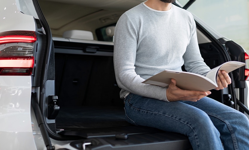 Extend the Life of Your Vehicle at West Broad VW in Richmond, VA |  Man in grey sweat shirt is sitting in SUV trunk while reading owners manual 