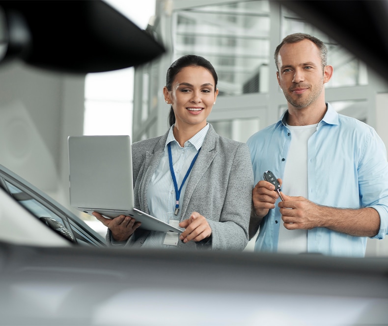 Enjoy A Test Drive At   West Broad VW in Richmond, VA | Man in blue shirt on the right is looking at a car with a sales person on the left side holding a clipboard