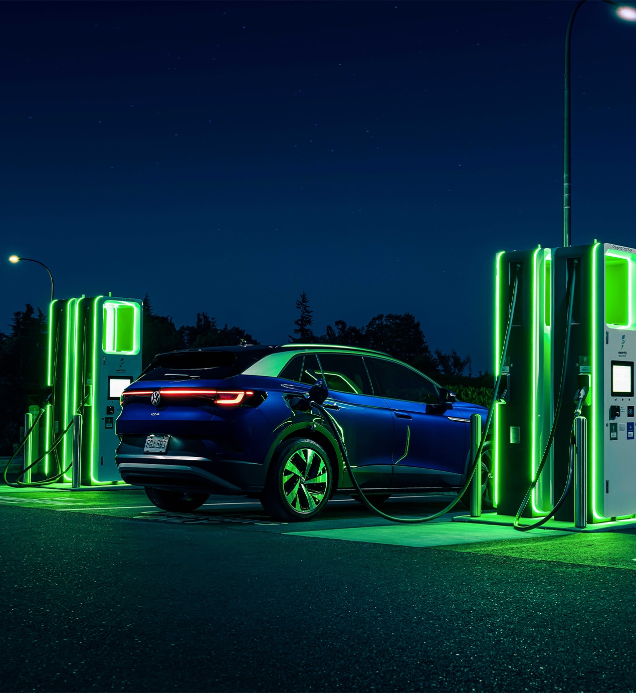 2023 ID.4 Electric SUV at West Broad VW | Navy Blue 2023 Volkswagen ID.4 parked next to car charger at night with neon green lights on charger