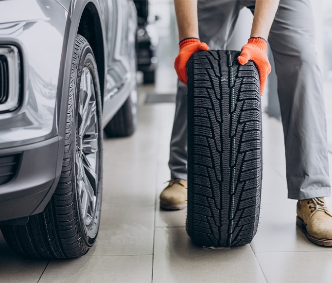 How to Get Your Car Summer Ready at West Broad VW in Richmond, VA | Man with orange gloves rolling brand new tire across floor